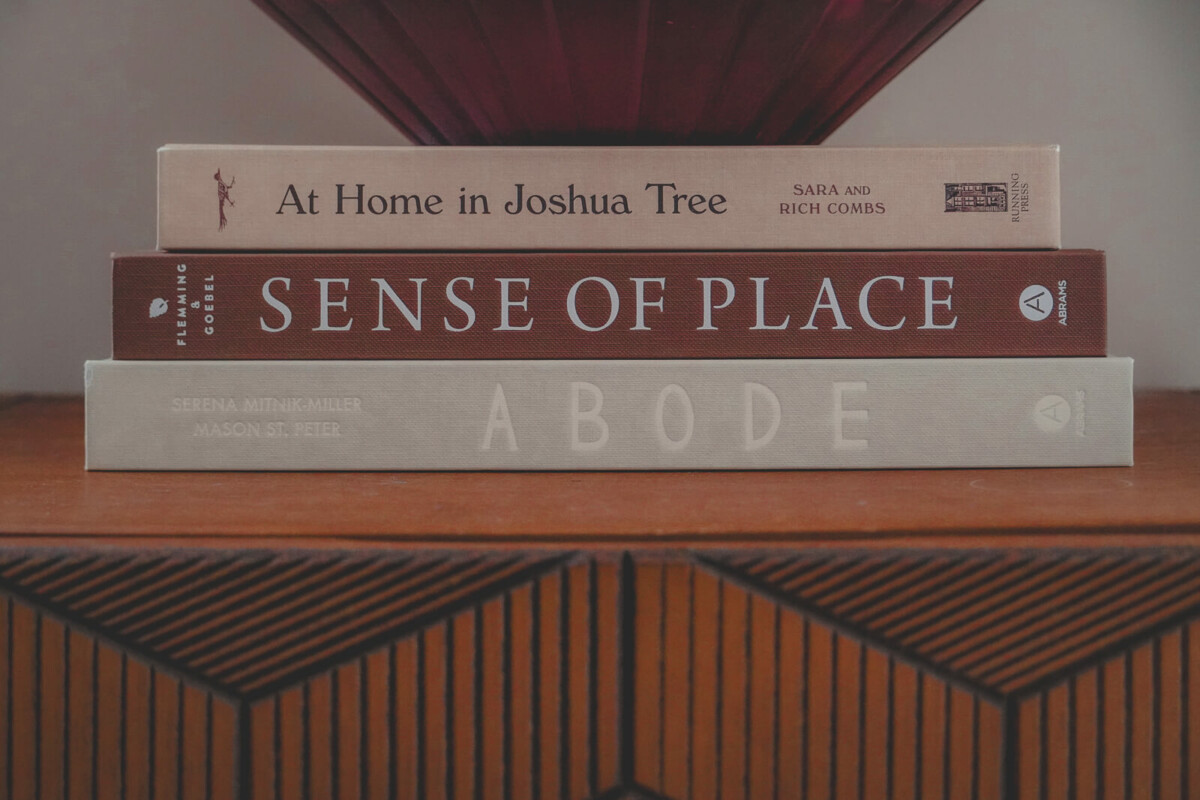 Travel coffee table books (At Home In Joshua Tree, Sense Of Place) styled in a stack of three on a shelf