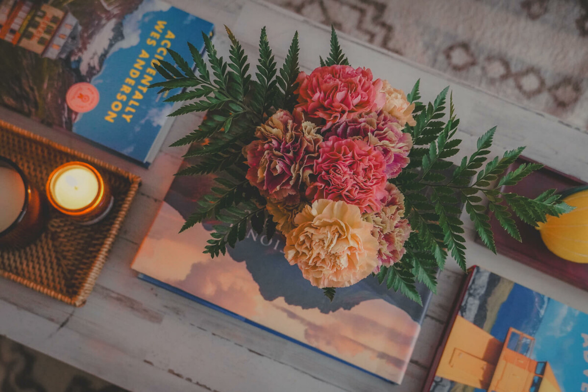 Coffee table styled with colorful flowers and warm candlelight and aesthetic travel photography coffee table books like Accidentally Wes Anderson and Our National Monuments