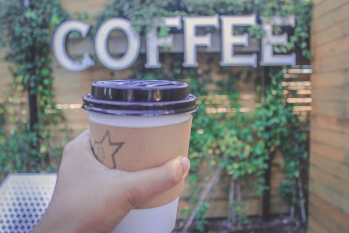holding a cup of coffee in front of a coffee sign