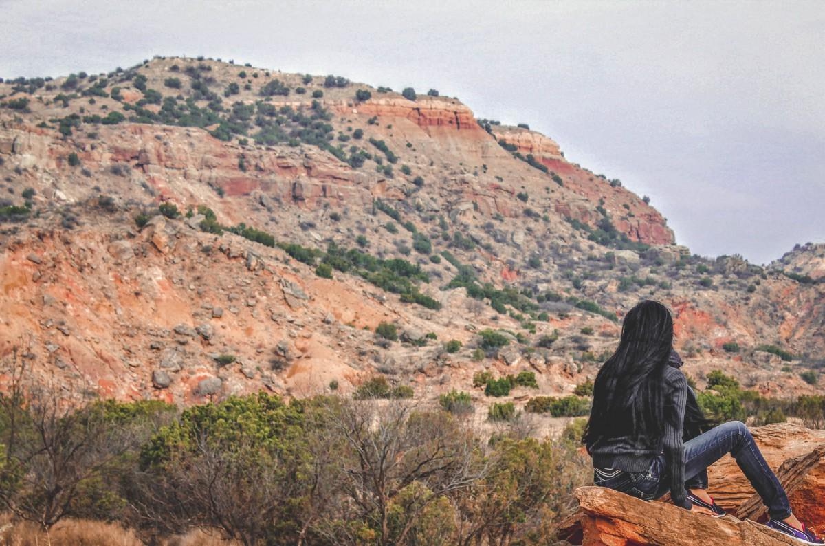 girl sitting on a ledge looking at Palo Duro Canyon 