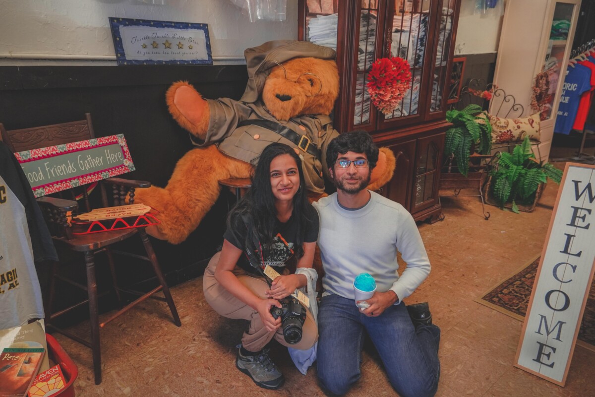 photo of Anshula and Vyas seated in Historic 4th Avenue Shirts in front. ofa giant teddy bear, signifying one of the shops in 4th Avenue Historic District