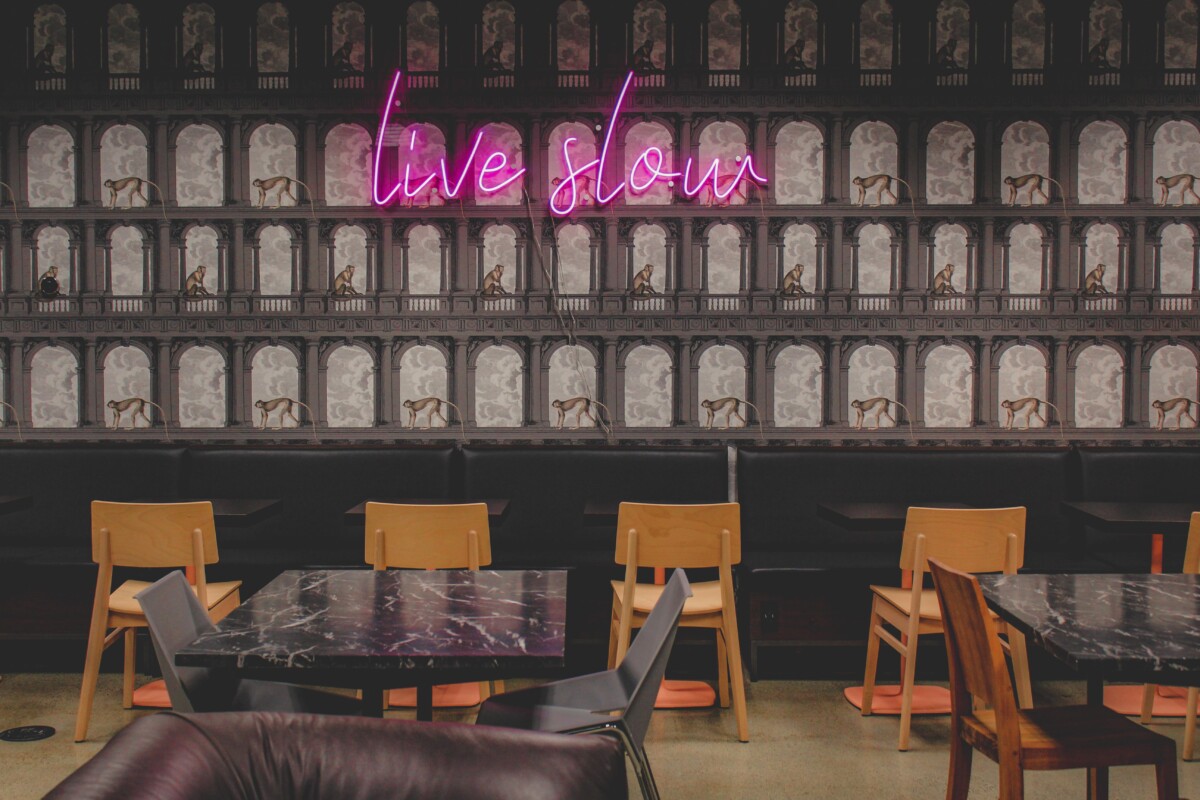 wallpapered wall at Jaho Coffee, pink neon sign that says Live Slow, and ample seating in the form of chairs and tables