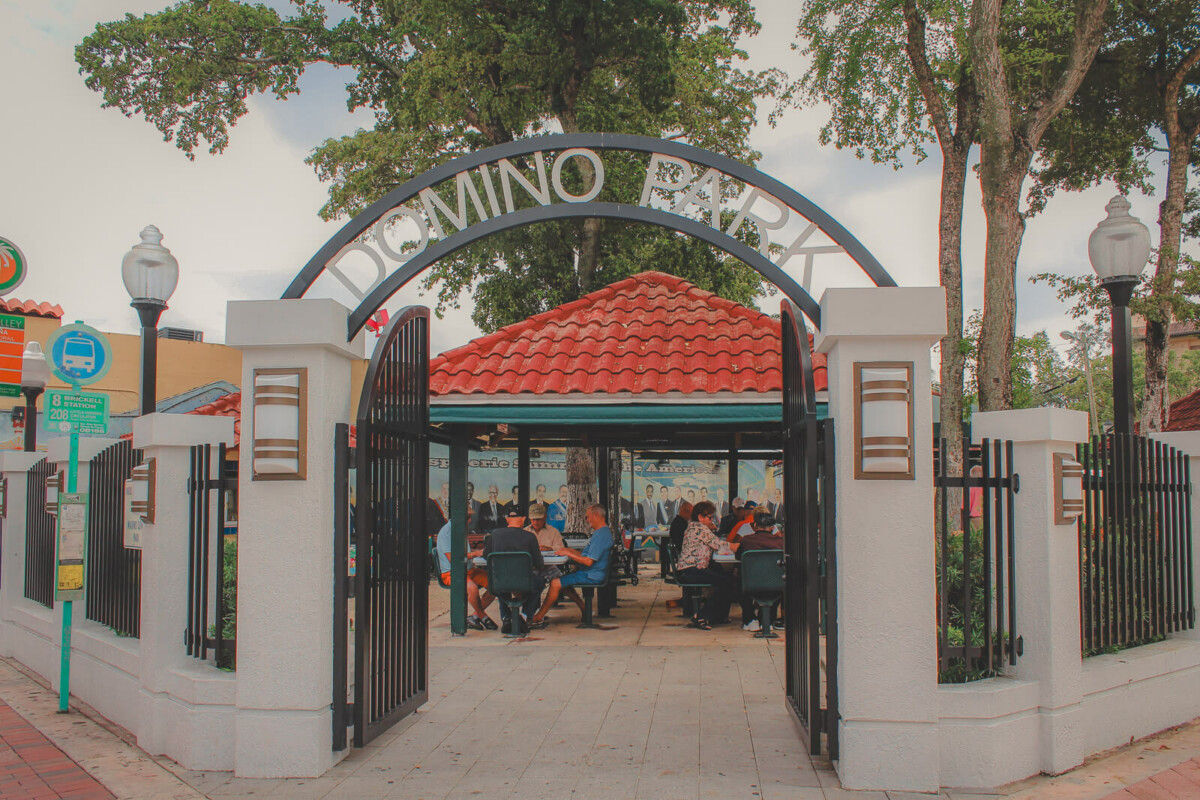 Domino Park entrance where people are playing dominoes at shaded tables