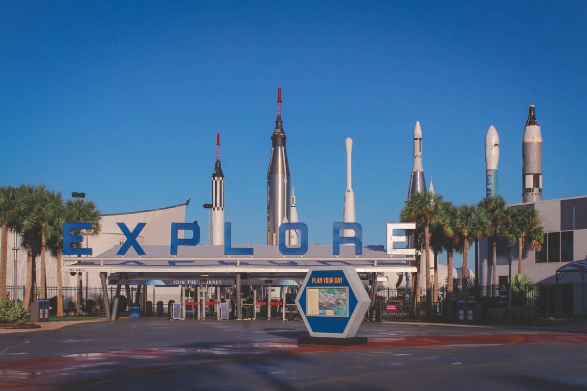 Kennedy Space Center tickets, cost and parking fee header image that shows entrance to KSC with rockets in the background and a plan your day sign